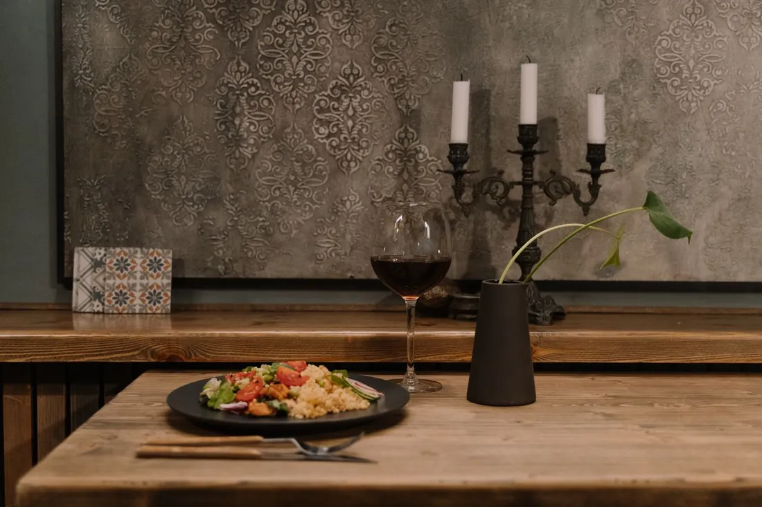 Table en bois rustique dressée avec une assiette et un verre de vin, ambiance conviviale d'un dîner chez l'habitant