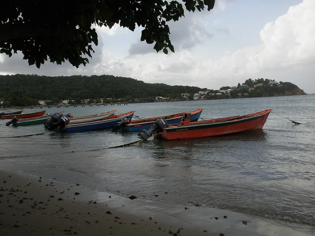 Barques de pêche colorées échouées sur la plage de Tartane, avec le village et les collines de la presqu'île de la Caravelle en arrière-plan