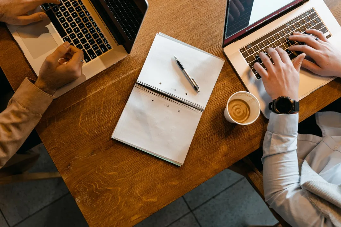 Deux personnes en coworking avec ordinateurs portables, carnet et café
