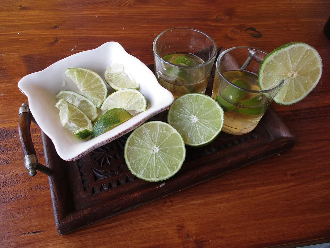 Deux verres de ti-punch au rhum avec des quartiers et des rondelles de citron vert sur un plateau en bois