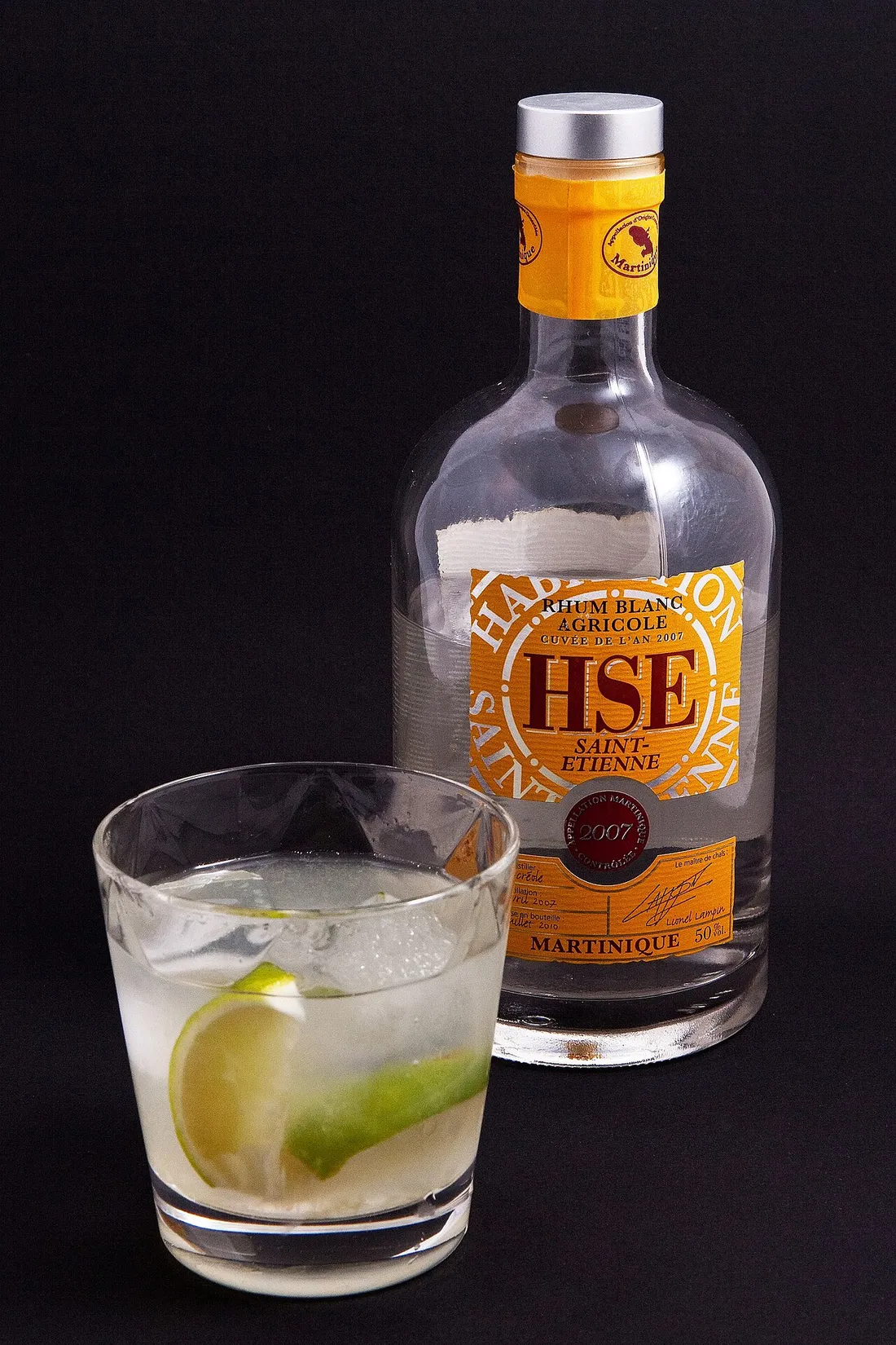 Verre de ti-punch avec quartier de citron vert servi a cote d'une bouteille de rhum blanc agricole HSE Saint-Etienne de Martinique