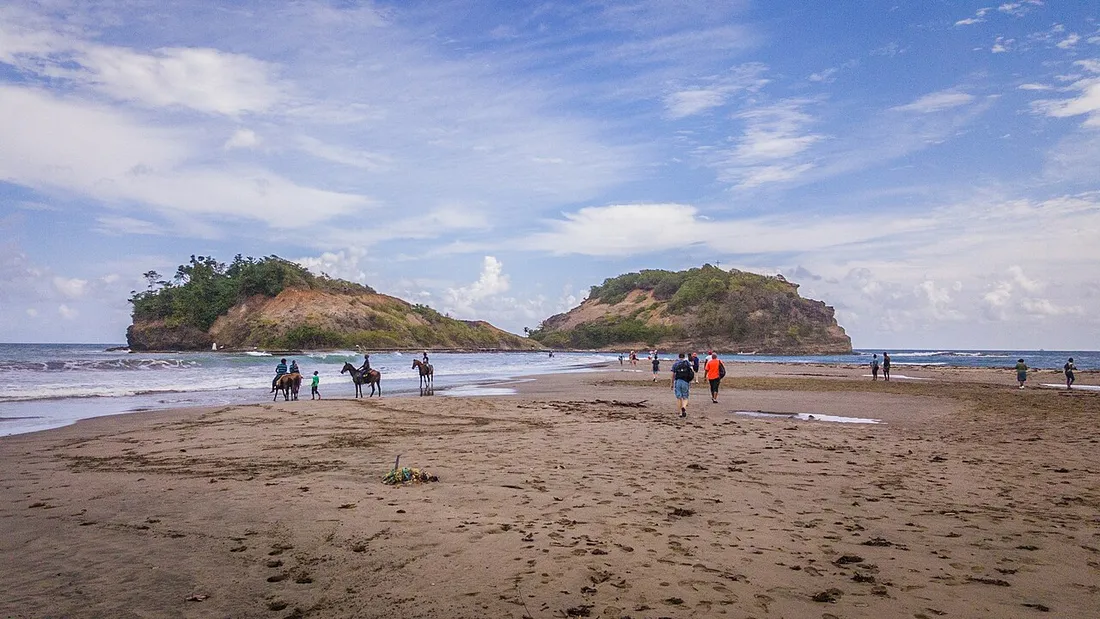 Promeneurs et cavaliers traversant à pied le banc de sable du tombolo de Sainte-Marie vers l'îlet à marée basse, en Martinique
