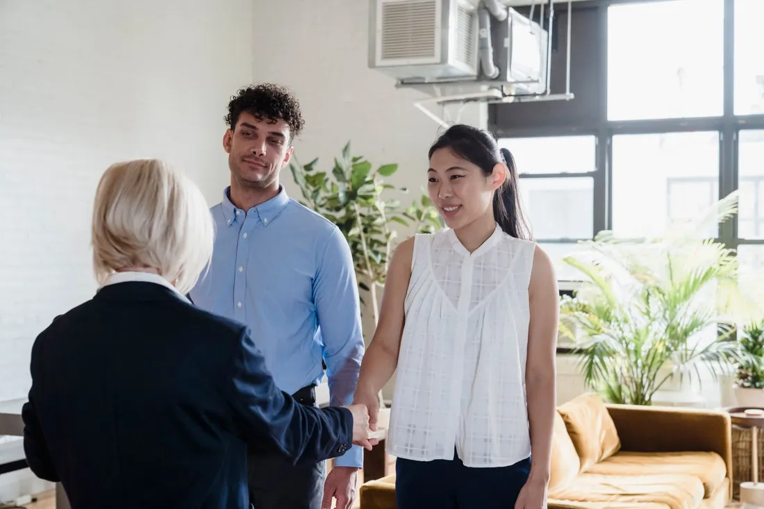 Un jeune couple serre la main d'une agente immobiliere dans un appartement lumineux