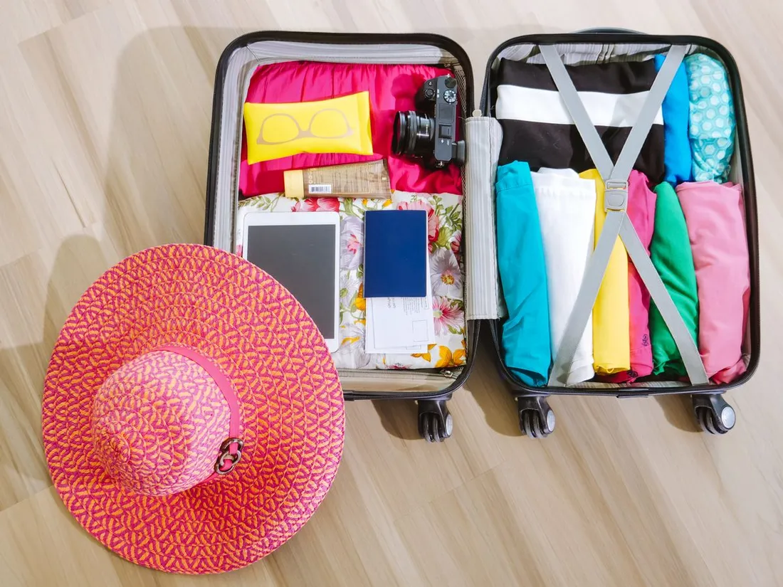 Valise ouverte et remplie pour un voyage tropical avec vêtements légers, chapeau de soleil, lunettes, crème solaire et passeport