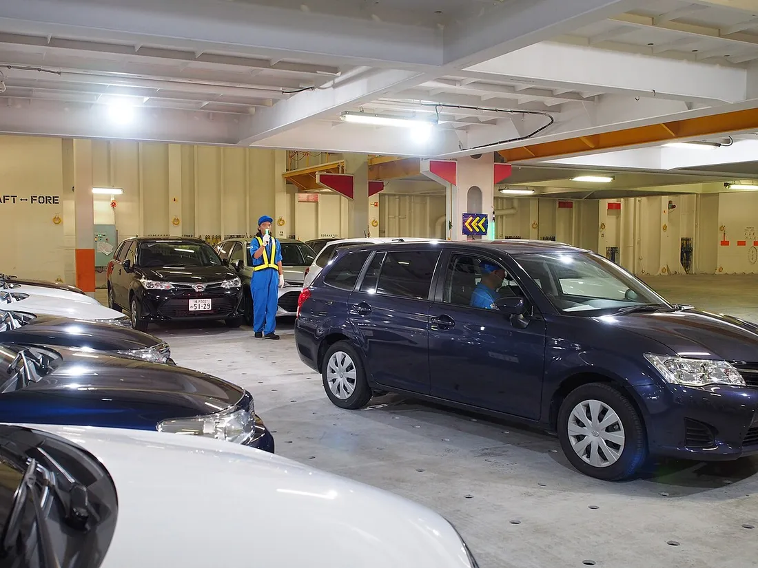 Voitures particulières arrimées sur le pont d'un navire roulier car-carrier, guidées par un membre d'équipage en combinaison bleue lors du chargement