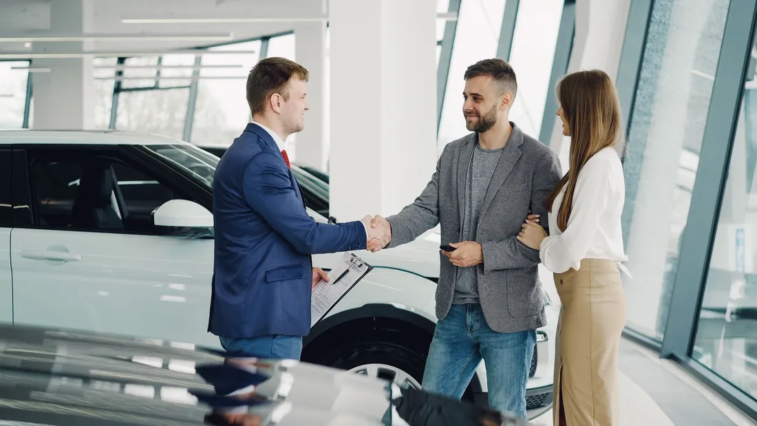 Un couple conclut l'achat d'une voiture en serrant la main d'un vendeur dans le hall d'une concession automobile