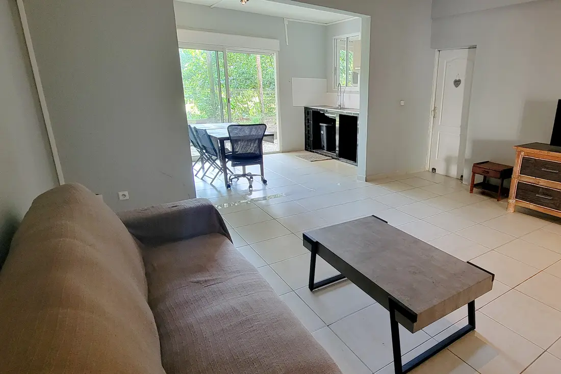 Séjour de la Villa Mahury : canapé, table basse, salle à manger devant la baie vitrée ouverte sur le jardin