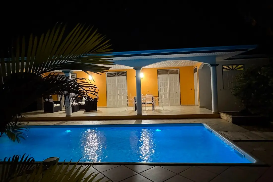 Piscine privée de la Villa Su Zen In éclairée de nuit, devant la façade jaune et la terrasse à colonnes