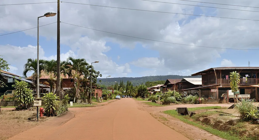 La rue principale du village de Cacao en Guyane, bordée de maisons hmong en bois et de palmiers, avec la forêt en arrière-plan