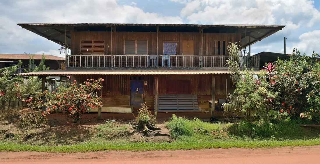 Maison hmong traditionnelle en bois à étage dans le village de Cacao, Guyane, entourée de végétation tropicale