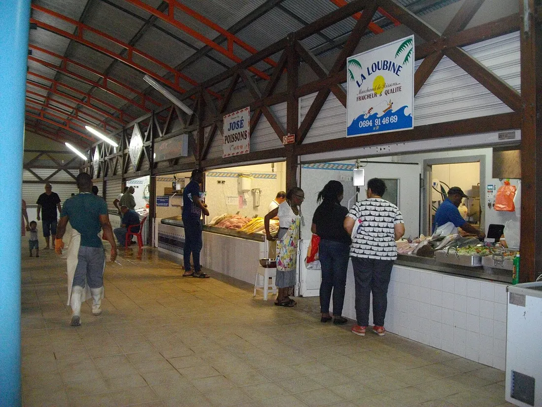 Halle du marché de Cayenne avec ses étals de poissons et ses clients sous la charpente métallique