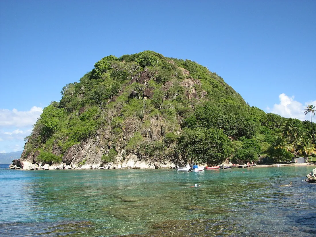 Le Pain de Sucre, colline conique boisée de Terre-de-Haut aux Saintes, bordée d'une eau turquoise avec quelques barques mouillées le long de la plage