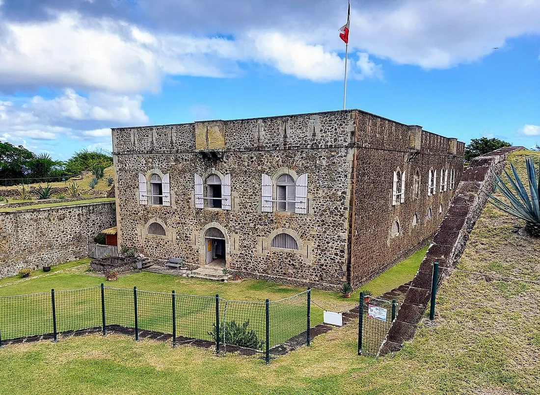 Le Fort Napoléon des Saintes à Terre-de-Haut, bâtisse fortifiée en pierre surmontée du drapeau français, entourée de remparts et d'un jardin d'agaves sous un ciel bleu