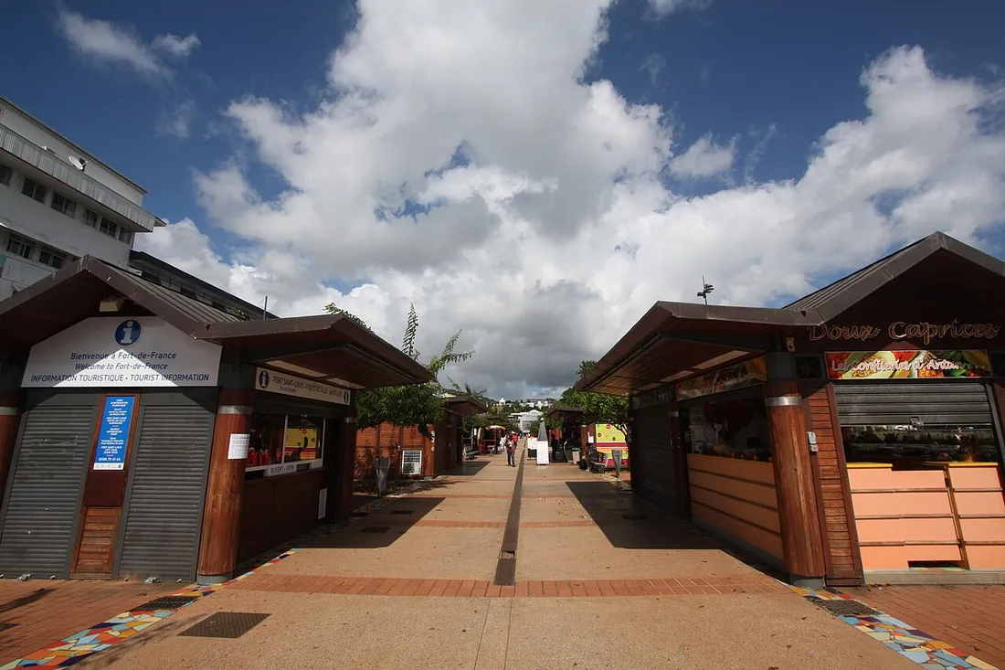 Allée de kiosques en bois du centre-ville de Fort-de-France, en Martinique, avec un panneau « Bienvenue à Fort-de-France » sous un ciel de nuages tropicaux