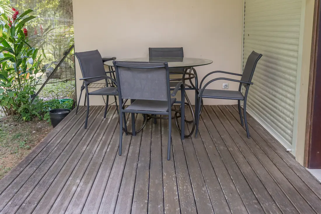 Terrasse en bois du T2 Mahury : table ronde en verre et quatre chaises devant le jardin tropical