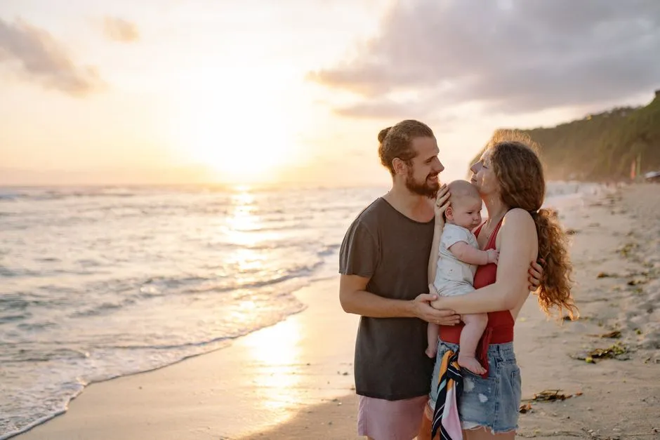 Jeune famille avec un bébé dans les bras sur une plage tropicale au coucher du soleil, en vacances