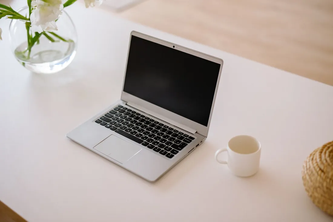 Ordinateur portable, tasse et bouquet de fleurs blanches sur un bureau épuré, ambiance espace de coworking