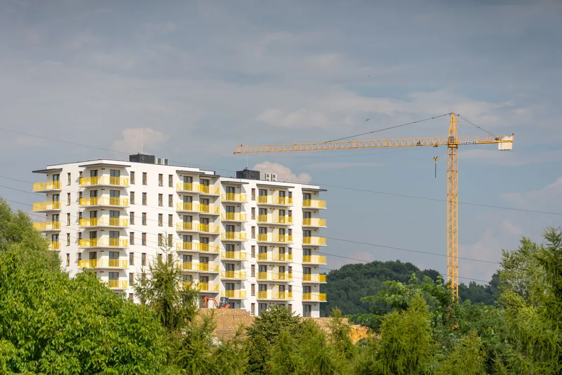 Immeuble de logements collectifs en cours d'achèvement, façade blanche et balcons jaunes sur huit niveaux, une grue à tour dressée à droite, végétation au premier plan